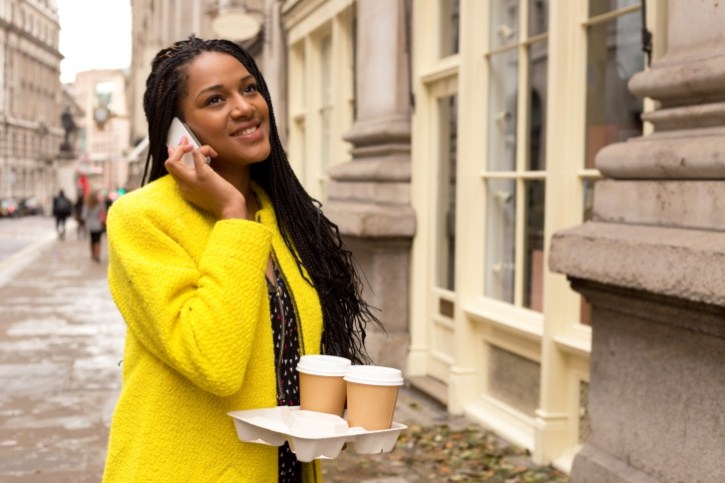 African American Black woman talking on cell phone outside carrying coffee