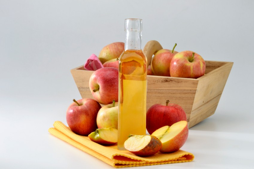 A bottle of apple cider vinegar and a basket filled with apples