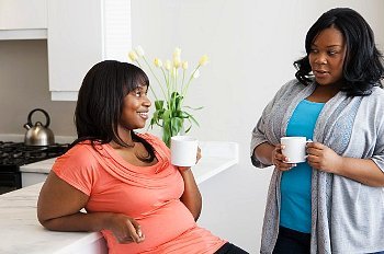 Two women talking to each other while standing near the kitchen