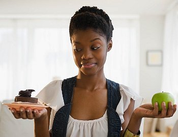 A woman choosing between chocolate cake and an apple