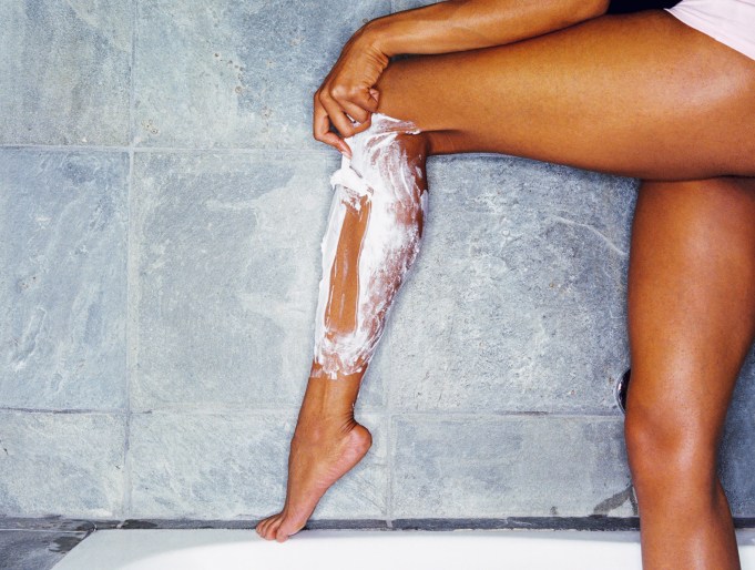 woman shaving legs with shaving cream and razor