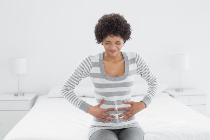 Casual woman with stomach pain sitting in bed