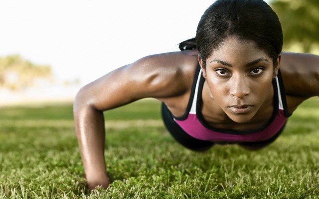 fit black woman doing push up outside on grass