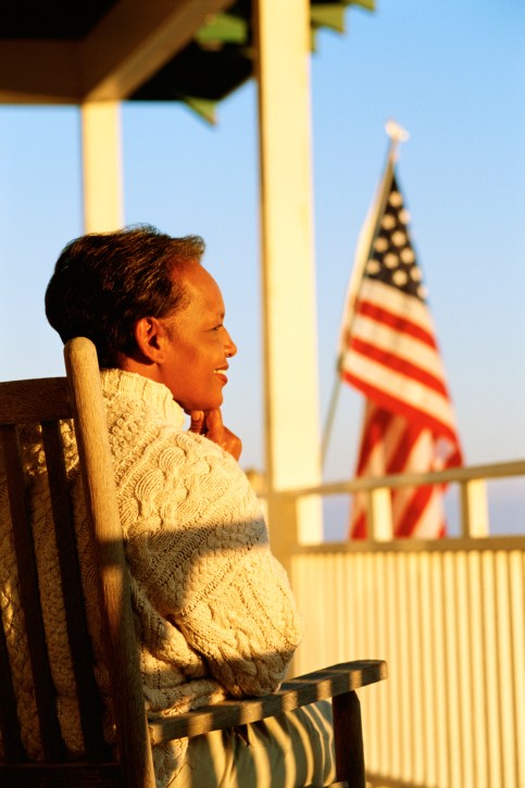 older black woman on porch in front of American flag smiling
