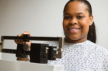 A woman wearing a hospital gown smiling while weighing herself.