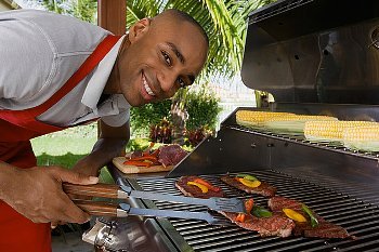 A man leaning over a grill full of steak and smiling