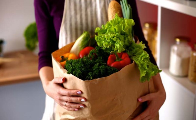 Young woman holding grocery shopping bag with vegetables